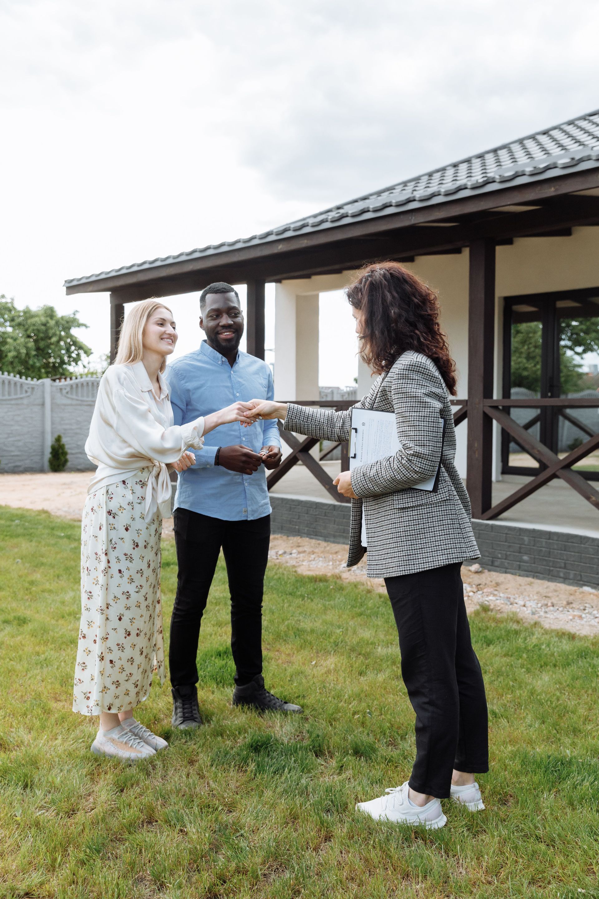 Three people shaking hands outside a house on a grassy lawn