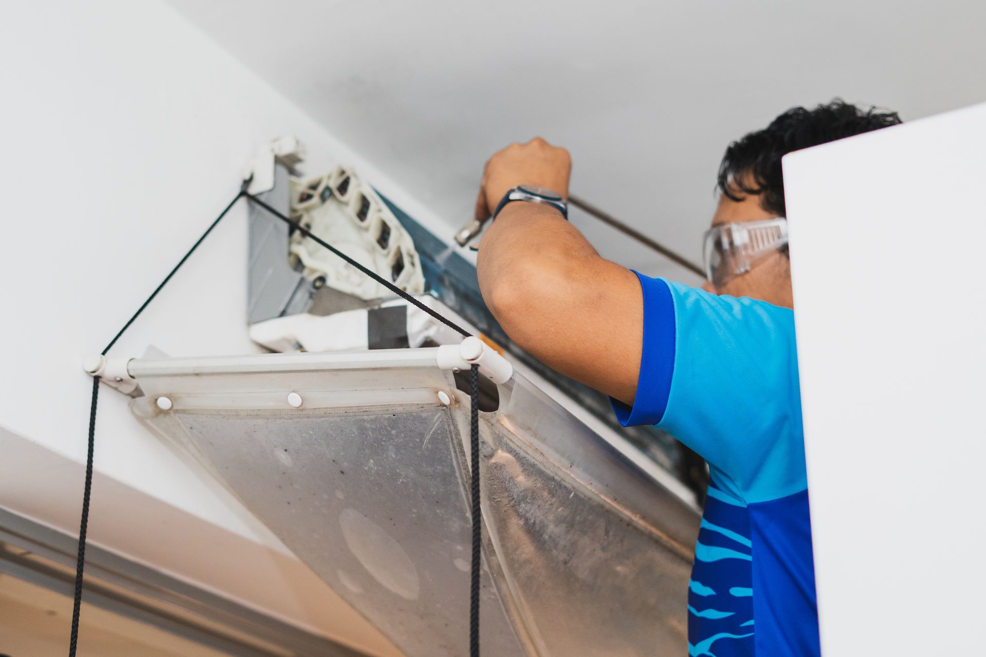 Technician in a blue shirt adjusting a ceiling fixture or panel on a wall-mounted bracket