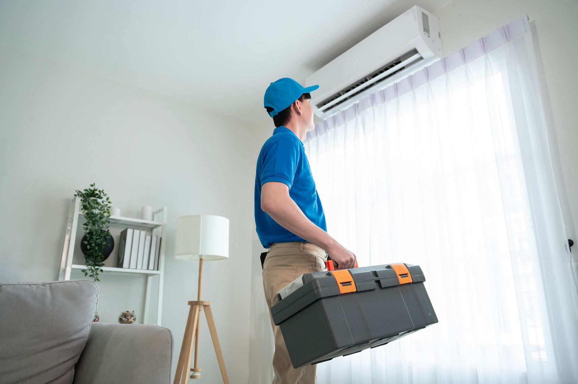 Technician carrying a toolbox beside a window in a bright living room