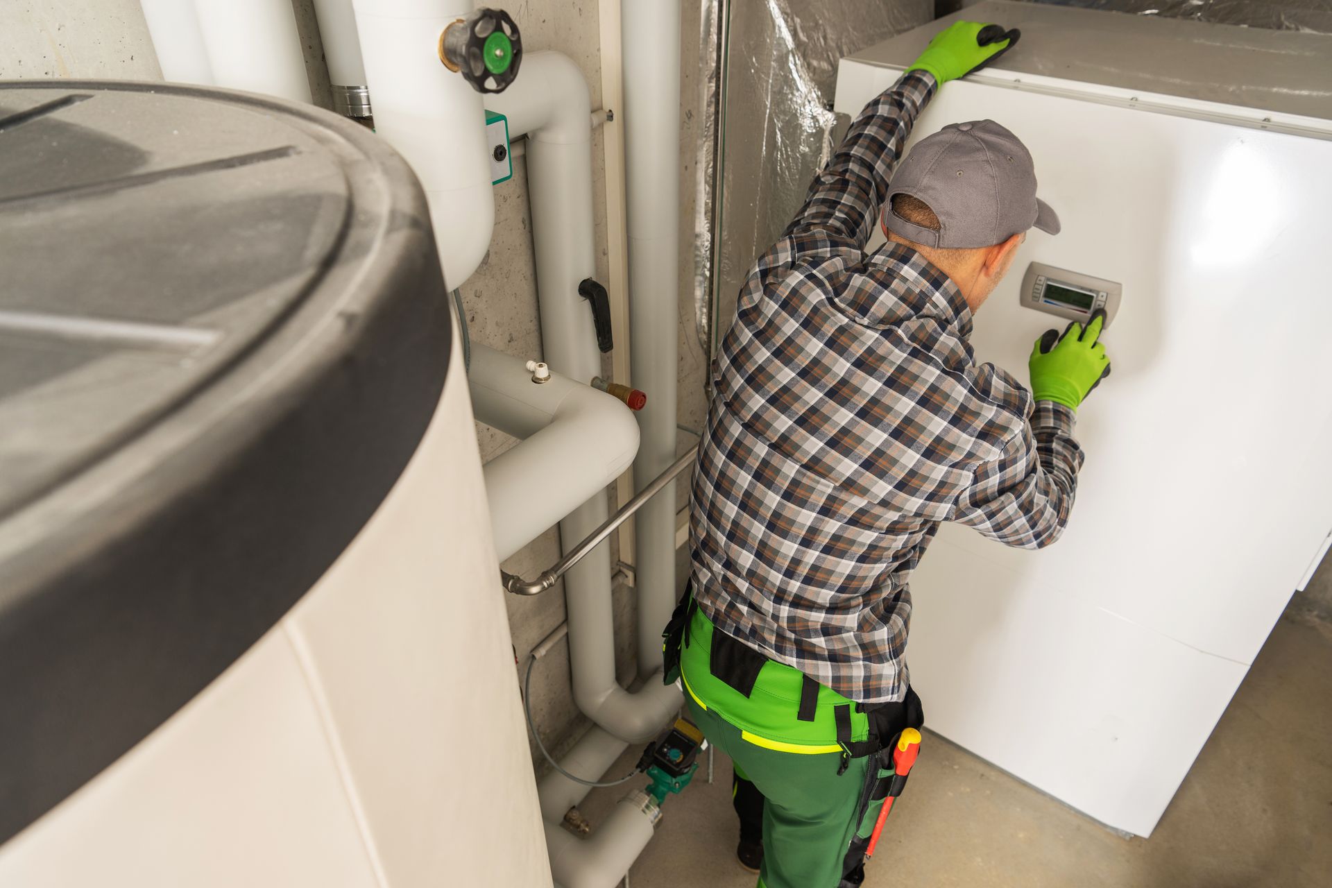Technician in green gloves inspecting a white appliance in a utility room next to large equipment.