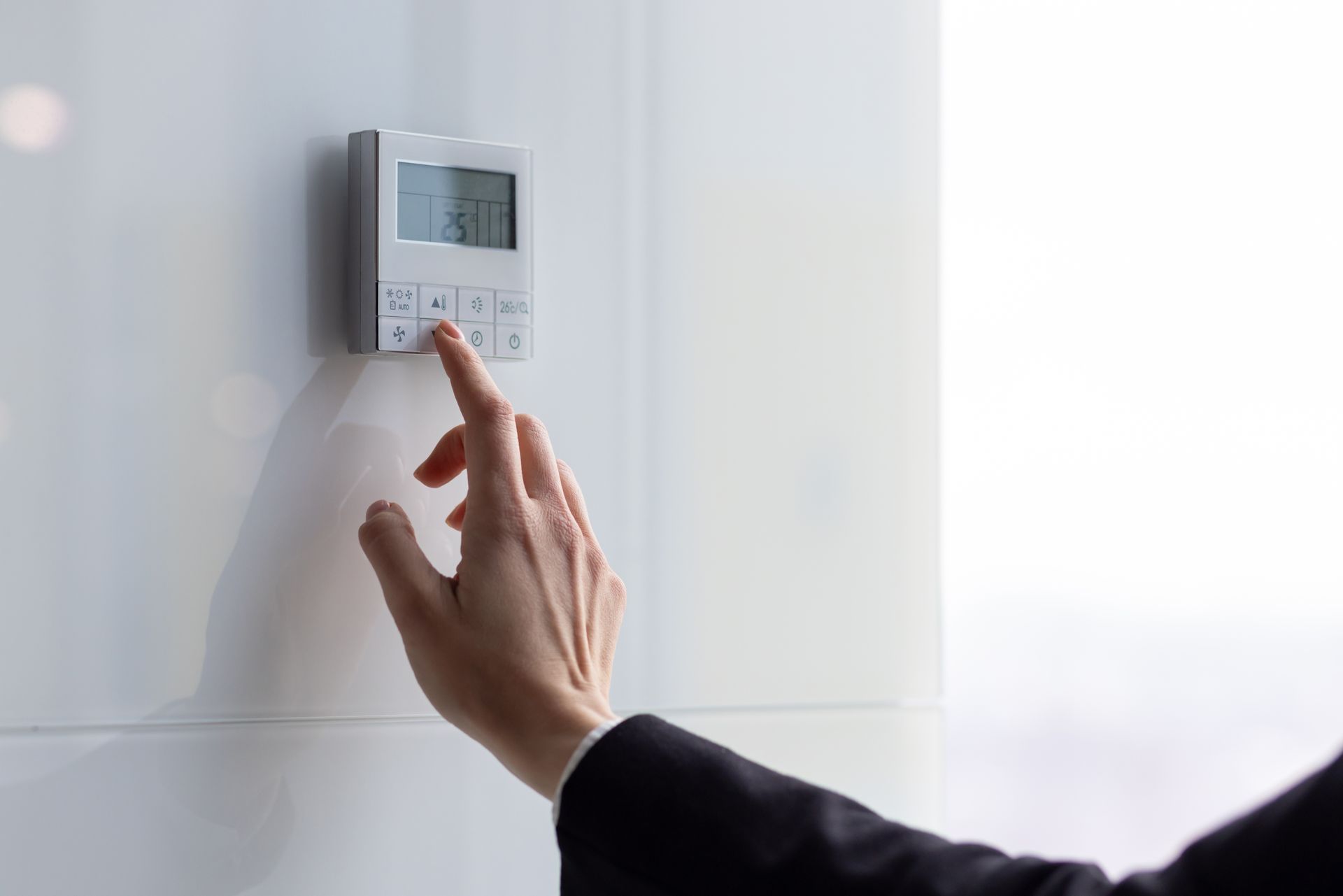 Hand adjusting a wall-mounted thermostat in a bright room