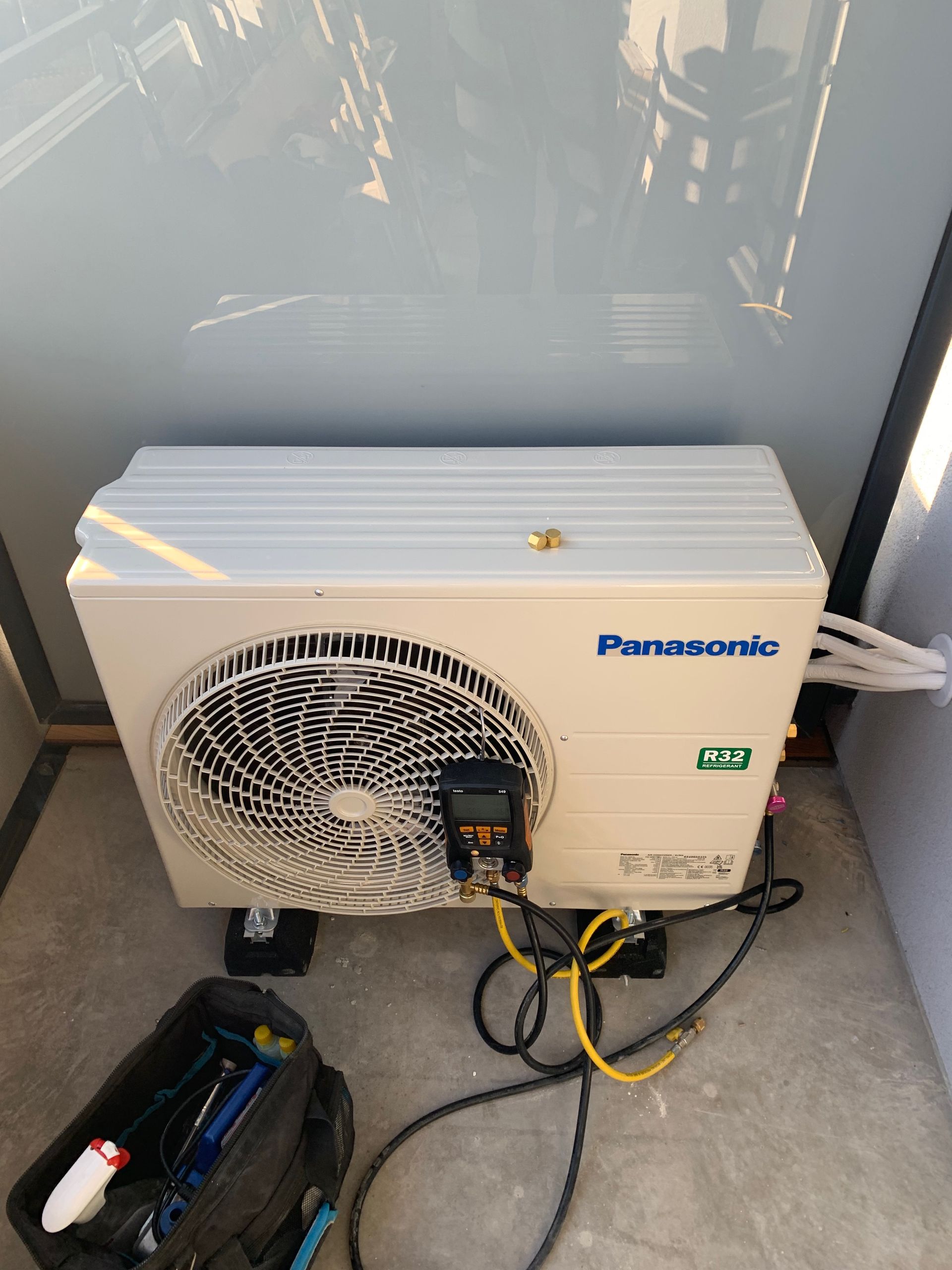 Klimatyzator Panasonic stoi na balkonie obok torby z narzędziami.