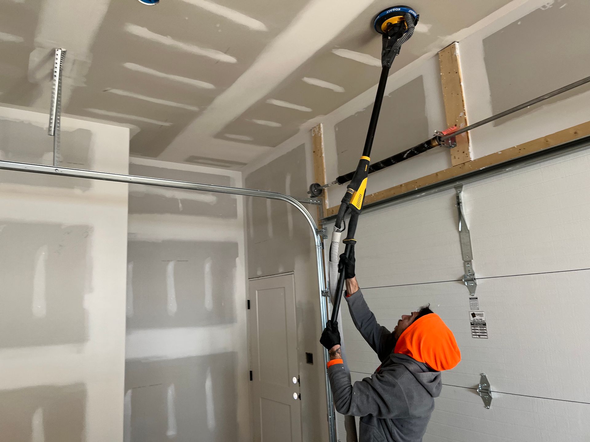 Person sanding a drywall ceiling in a garage using a long-handled sander.