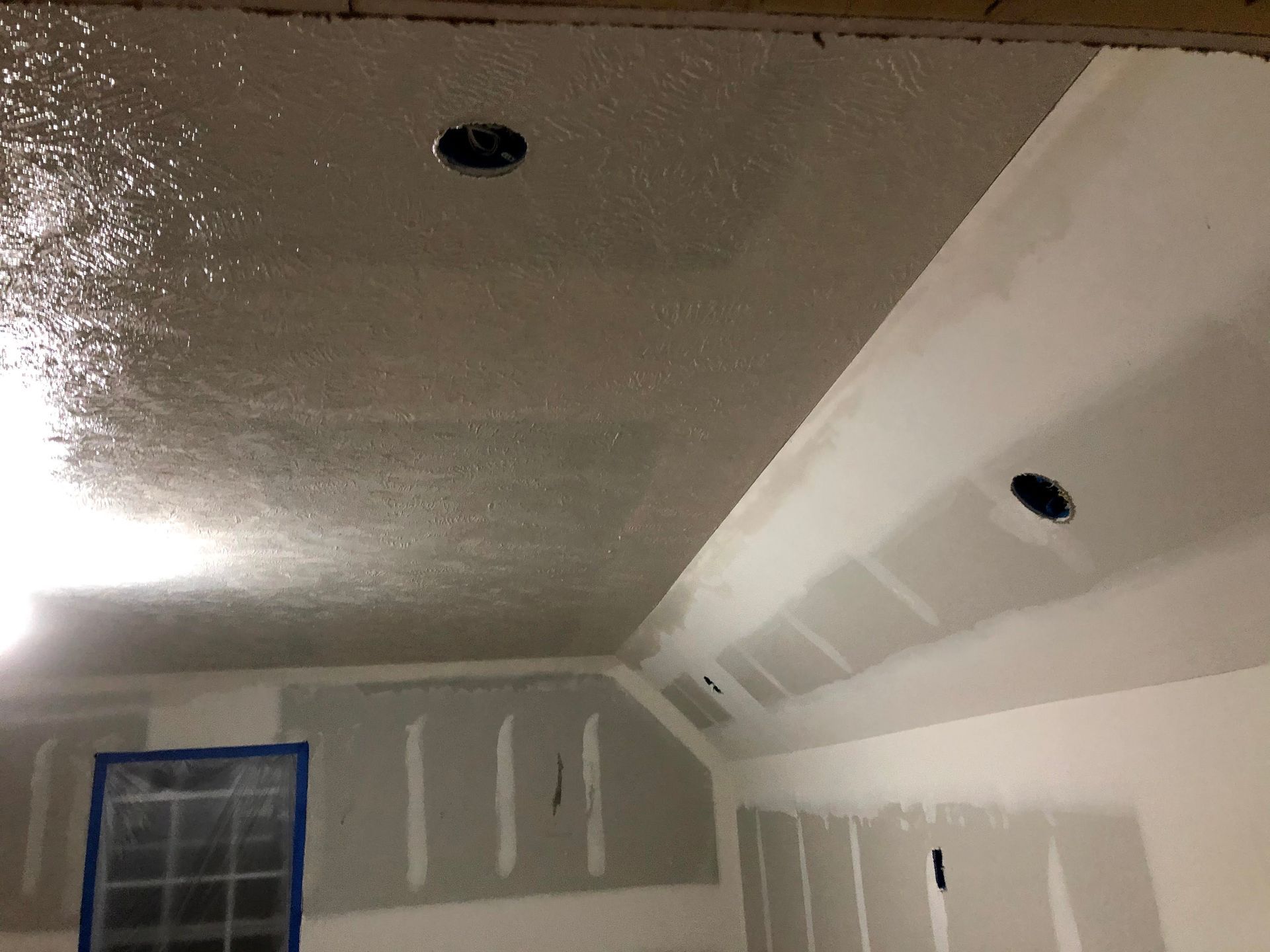 Ceiling drywall with two recessed lights. Walls with drywall partially installed; room under construction.