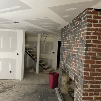 Interior construction site with exposed brick fireplace, drywall, and unfinished staircase.