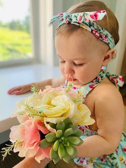 Toddler in floral dress and headband holding a bouquet by a bright window