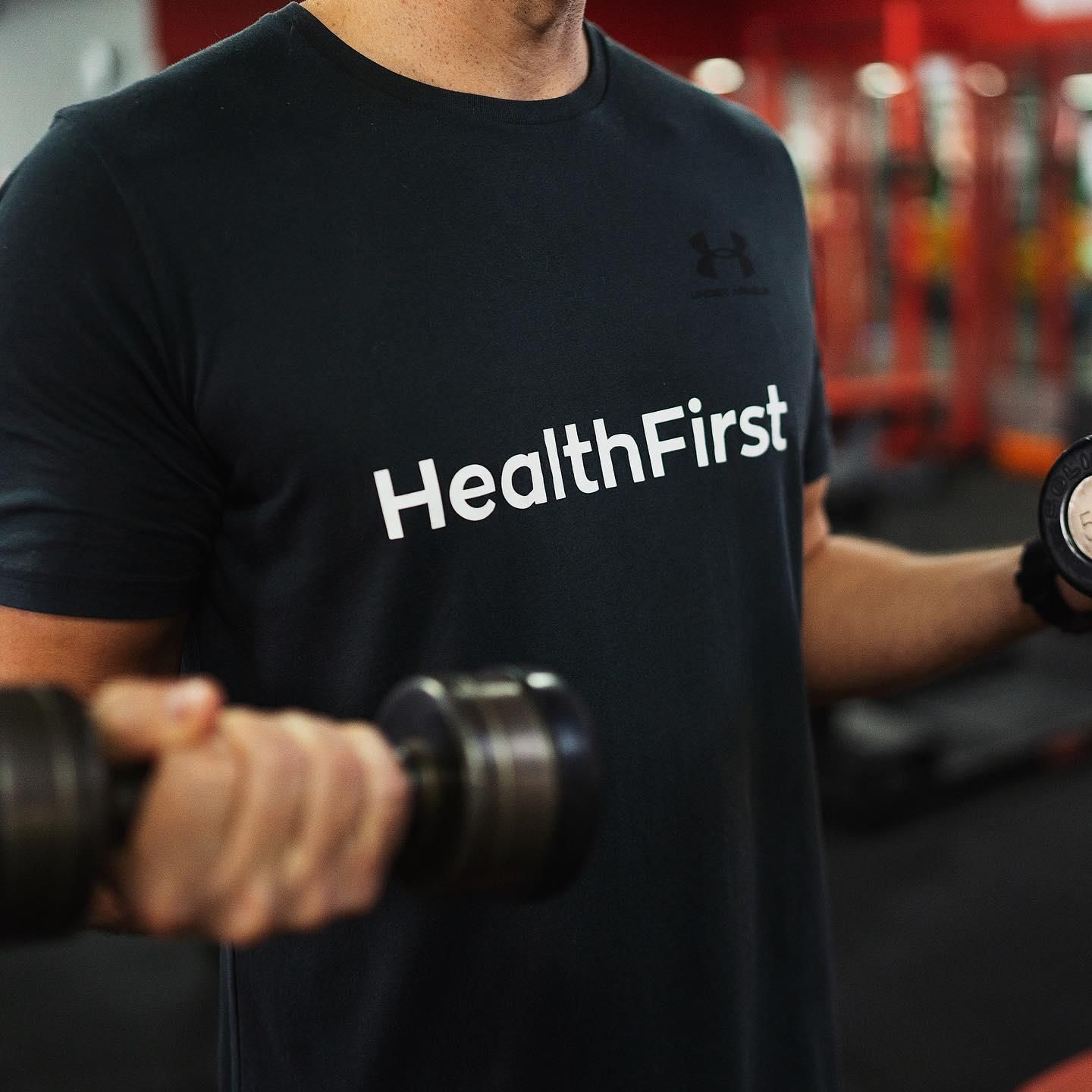 A Man is Squatting With a Barbell in a Gym — Health First Townsville In Townsville, QLD