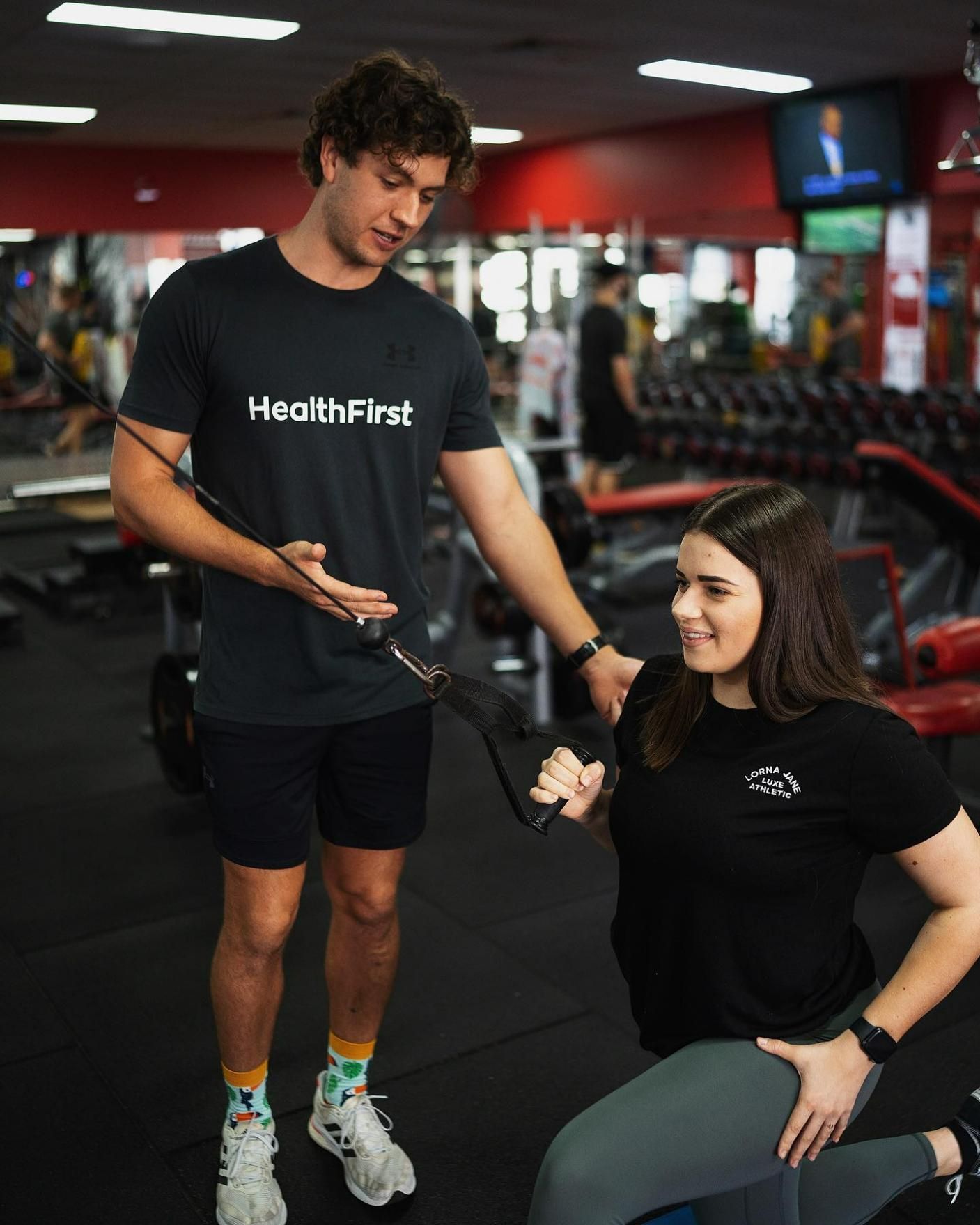A Man is Helping a Woman Do Exercises in a Gym — Health First Townsville In Townsville, QLD