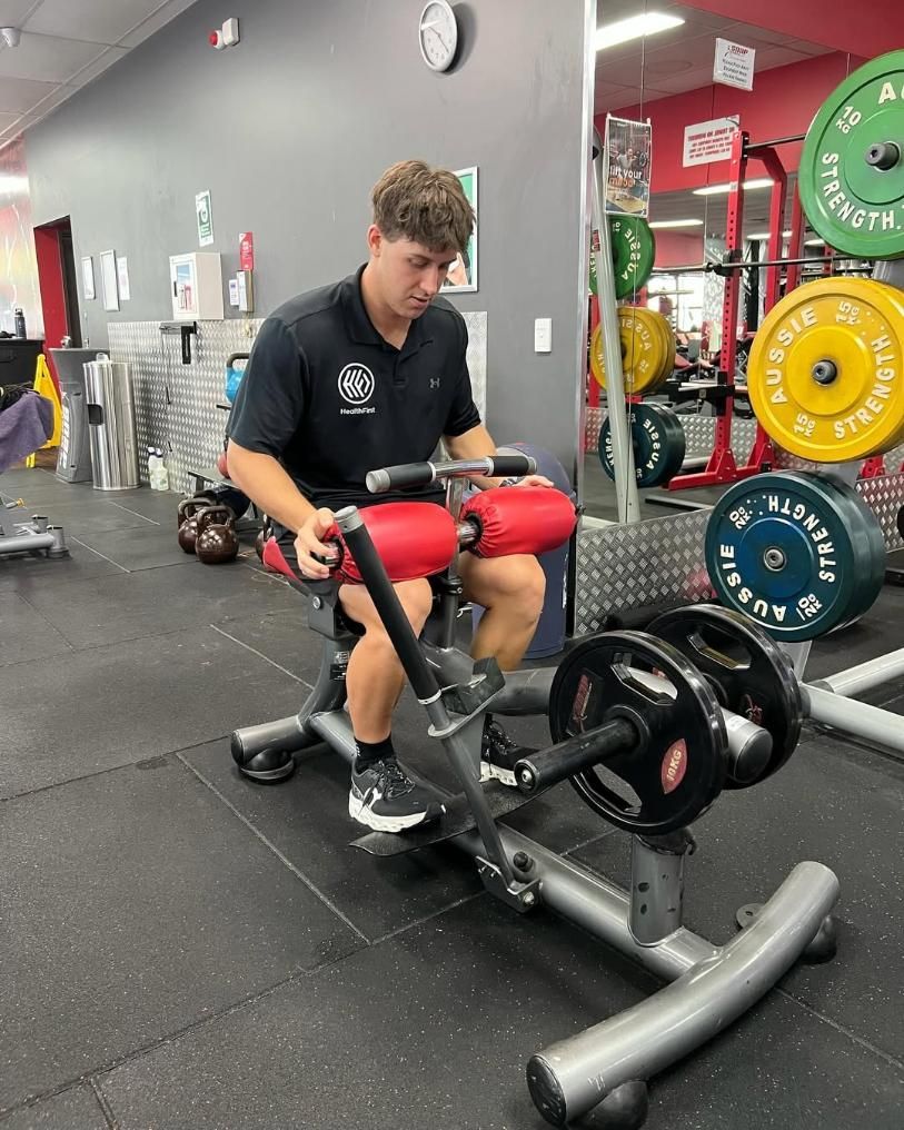 A Man is Sitting on a Machine in a Gym — Health First Townsville In Townsville, QLD