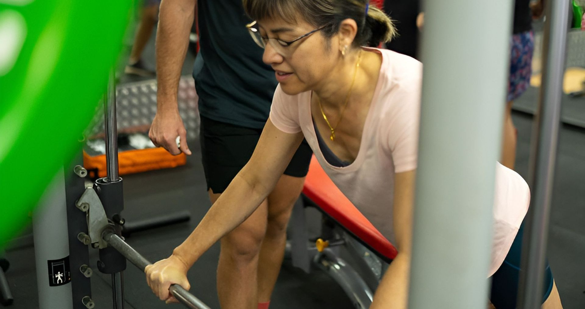 A Man is Helping a Woman Lift a Barbell in a Gym — Health First Townsville In Townsville, QLD