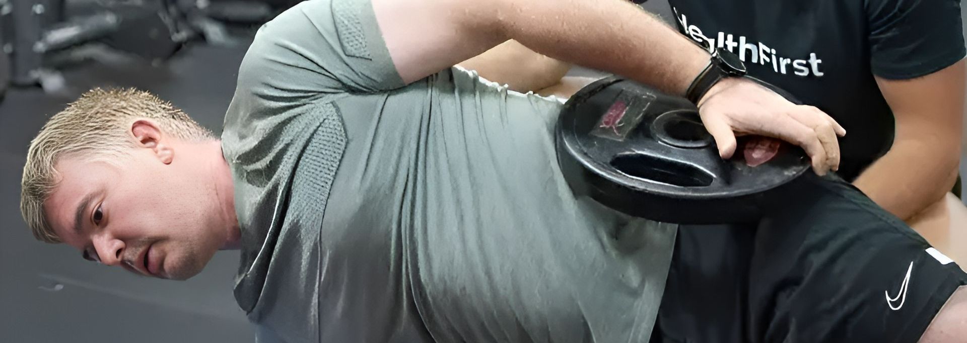 A Man is Laying on the Floor With a Barbell on His Back — Health First Townsville In Townsville, QLD