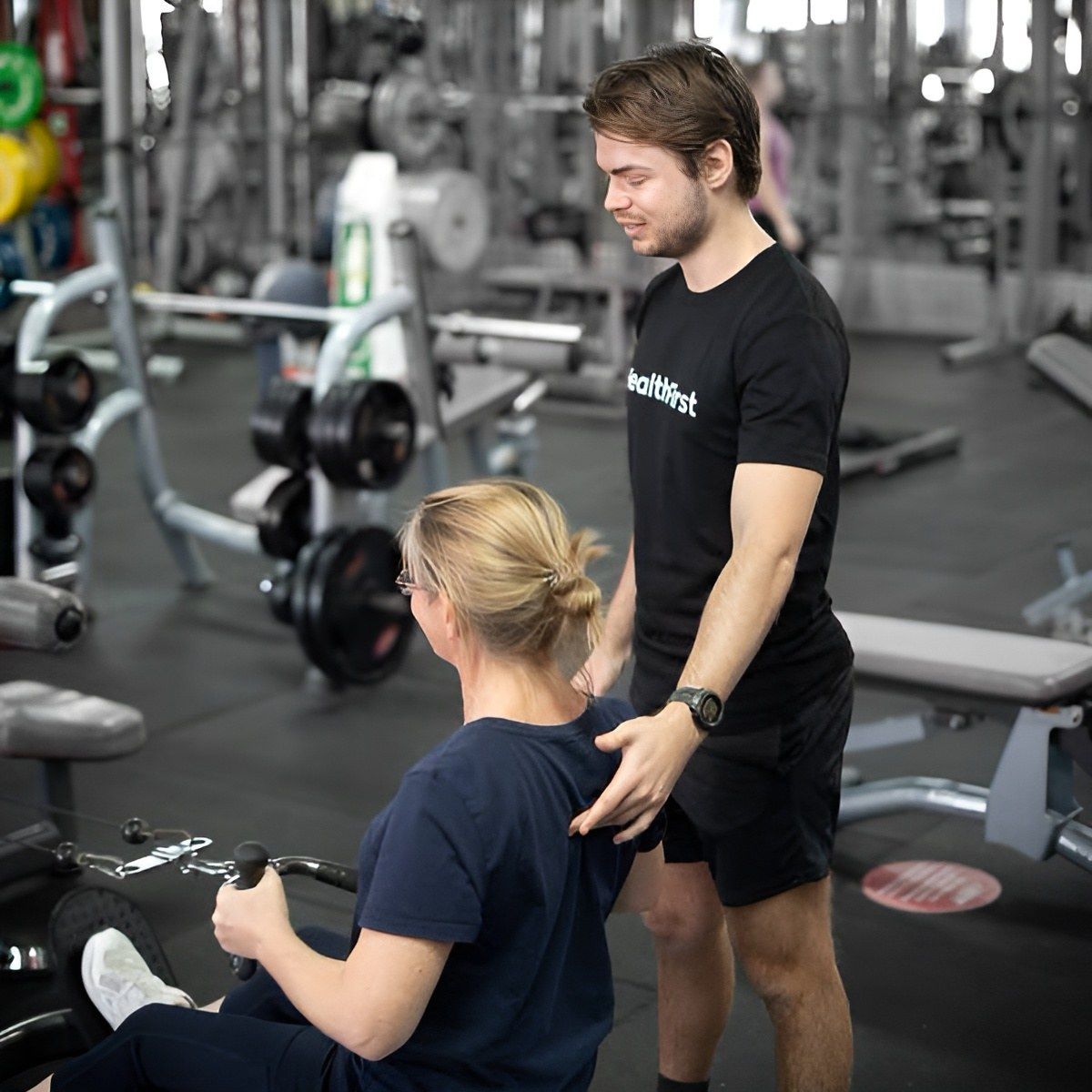 A Fitness Trainer Assisting a Person on a Rowing Machine in a Gym — Health First Townsville In Townsville, QLD