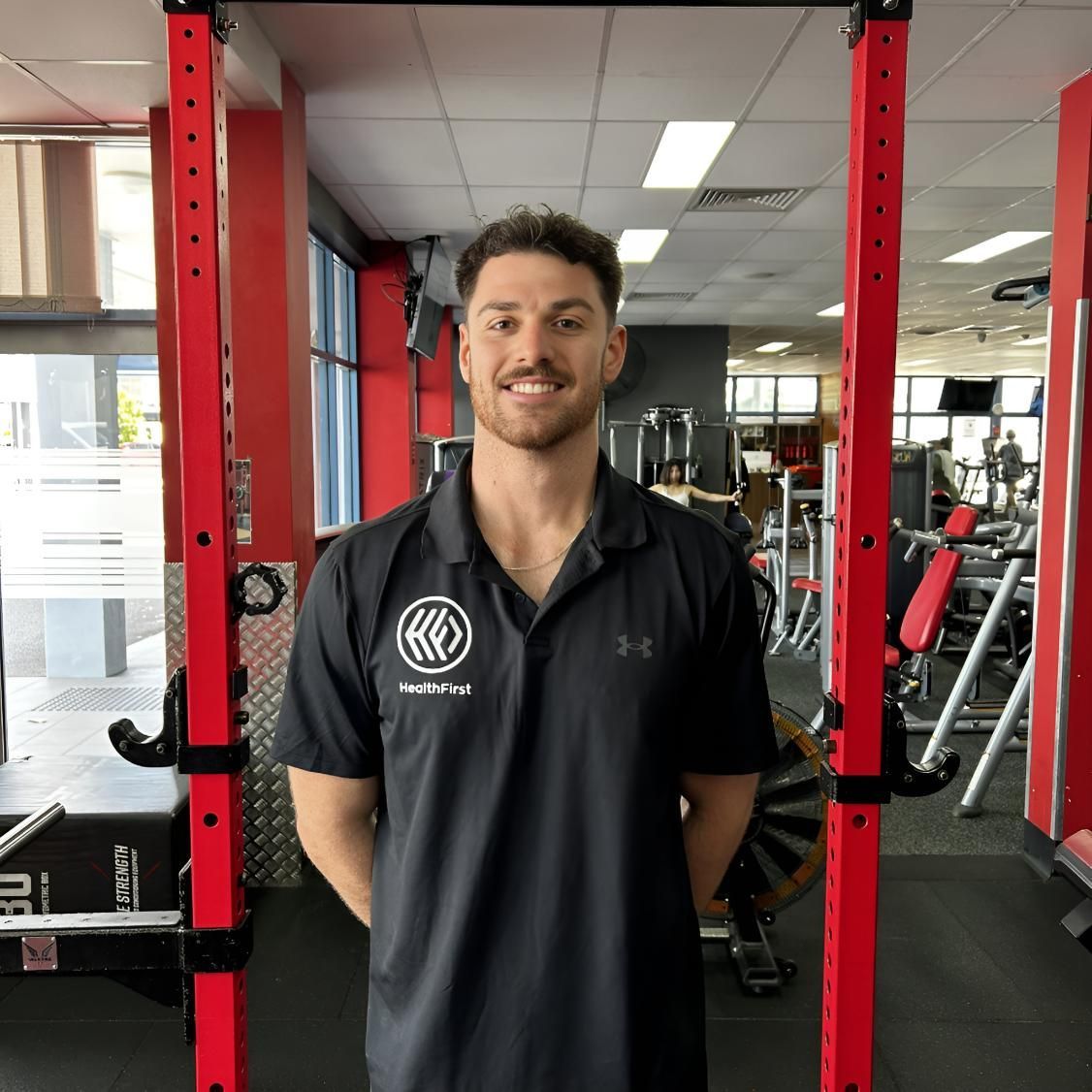 A Man in a Black Shirt is Standing in Front of a Red Bar in a Gym — Health First Townsville In Townsville, QLD