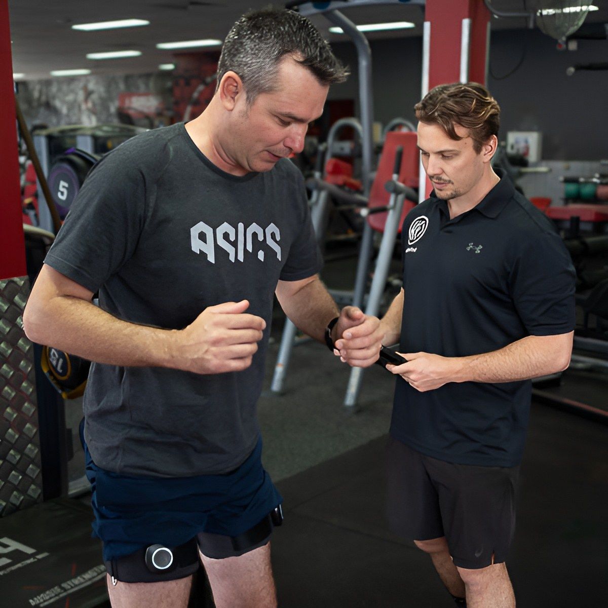 A Man Wearing an Asics Shirt Talks to Another Man in a Gym — Health First Townsville In Aitkenvale, QLD
