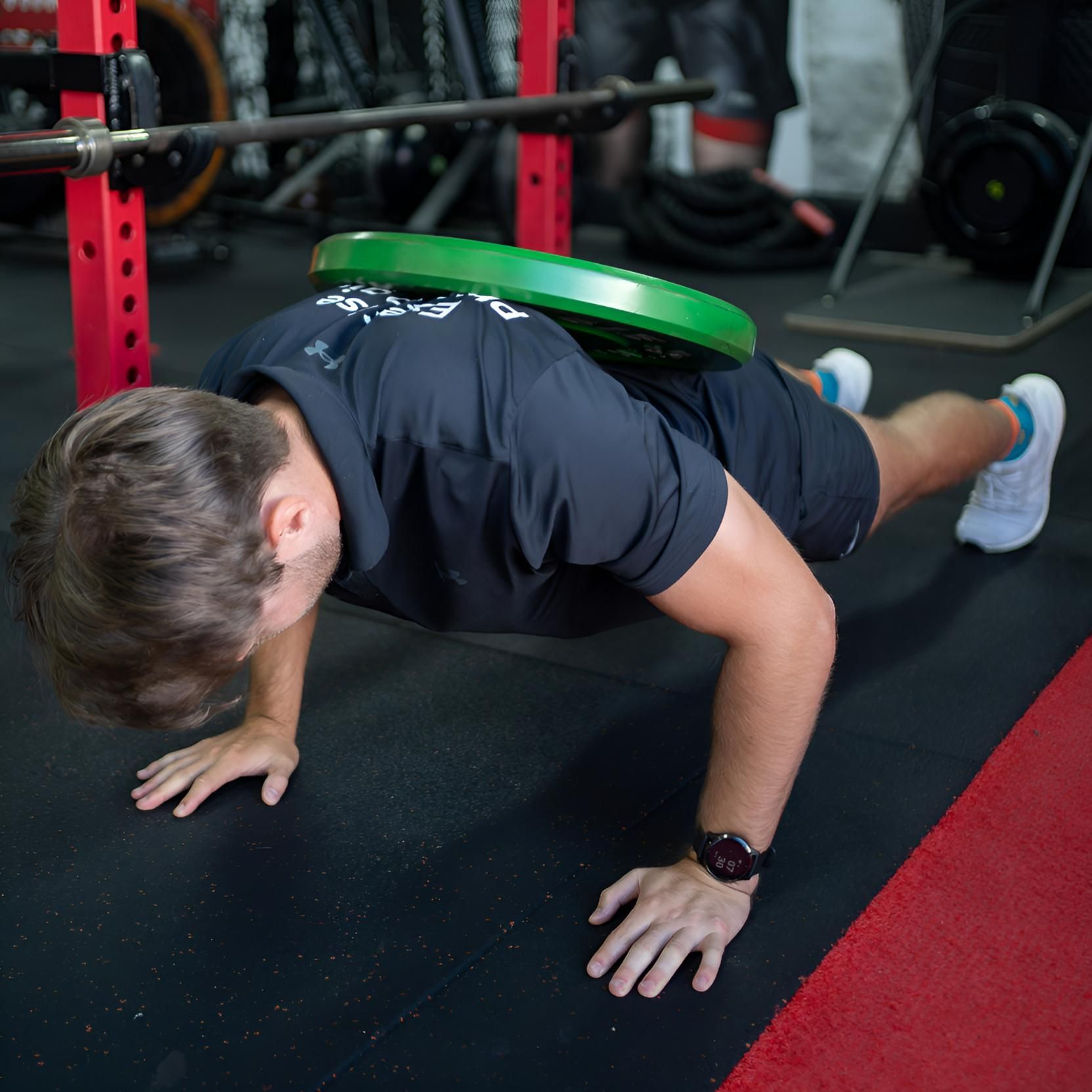 A Man is Doing Push Ups With a Green Plate on His Back — Health First Townsville In Townsville, QLD