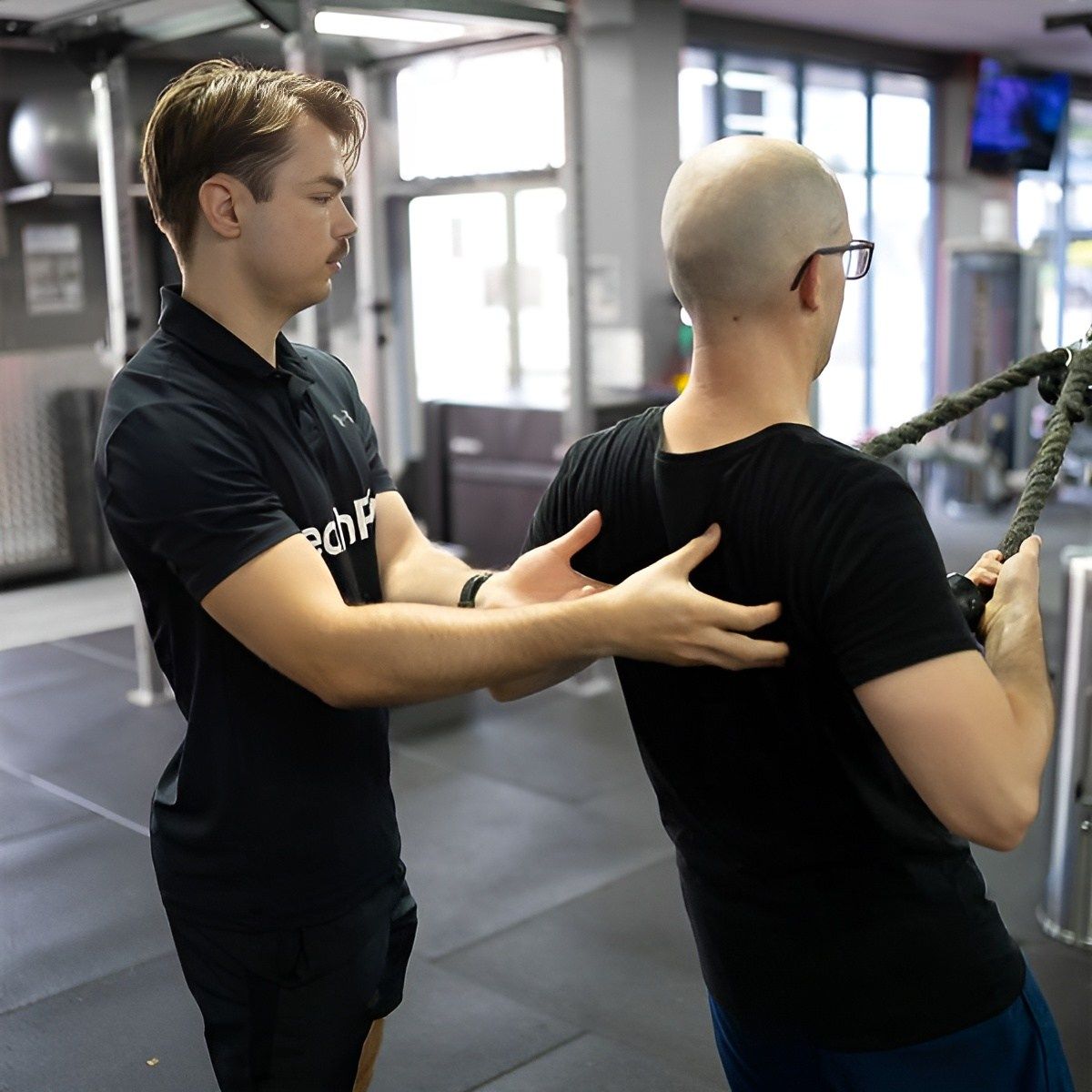A Man is Helping Another Man Lift a Rope in a Gym — Health First Townsville In Townsville, QLD