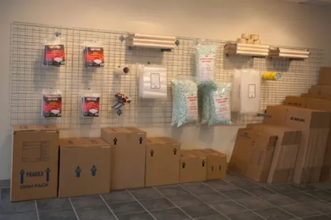 Store wall display with boxed merchandise, hanging organizers, and packaged items above stacked cardboard boxes.
