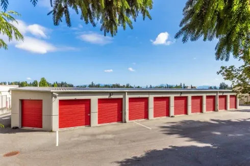 Row of red storage unit doors in a low white building under a clear blue sky