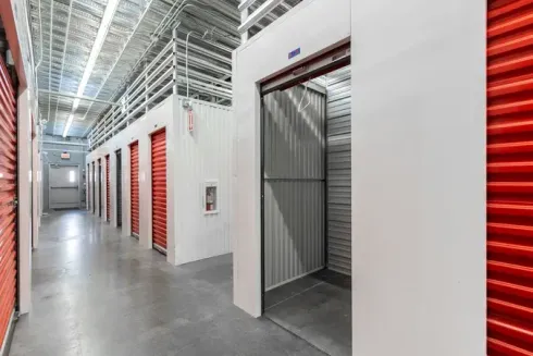 Interior of a self-storage facility with rows of red storage unit doors and one open unit hallway