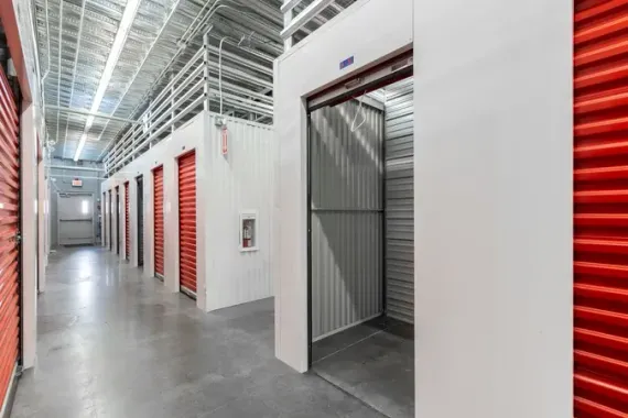 Inside a self-storage facility with red roll-up doors and one open unit along a polished hallway