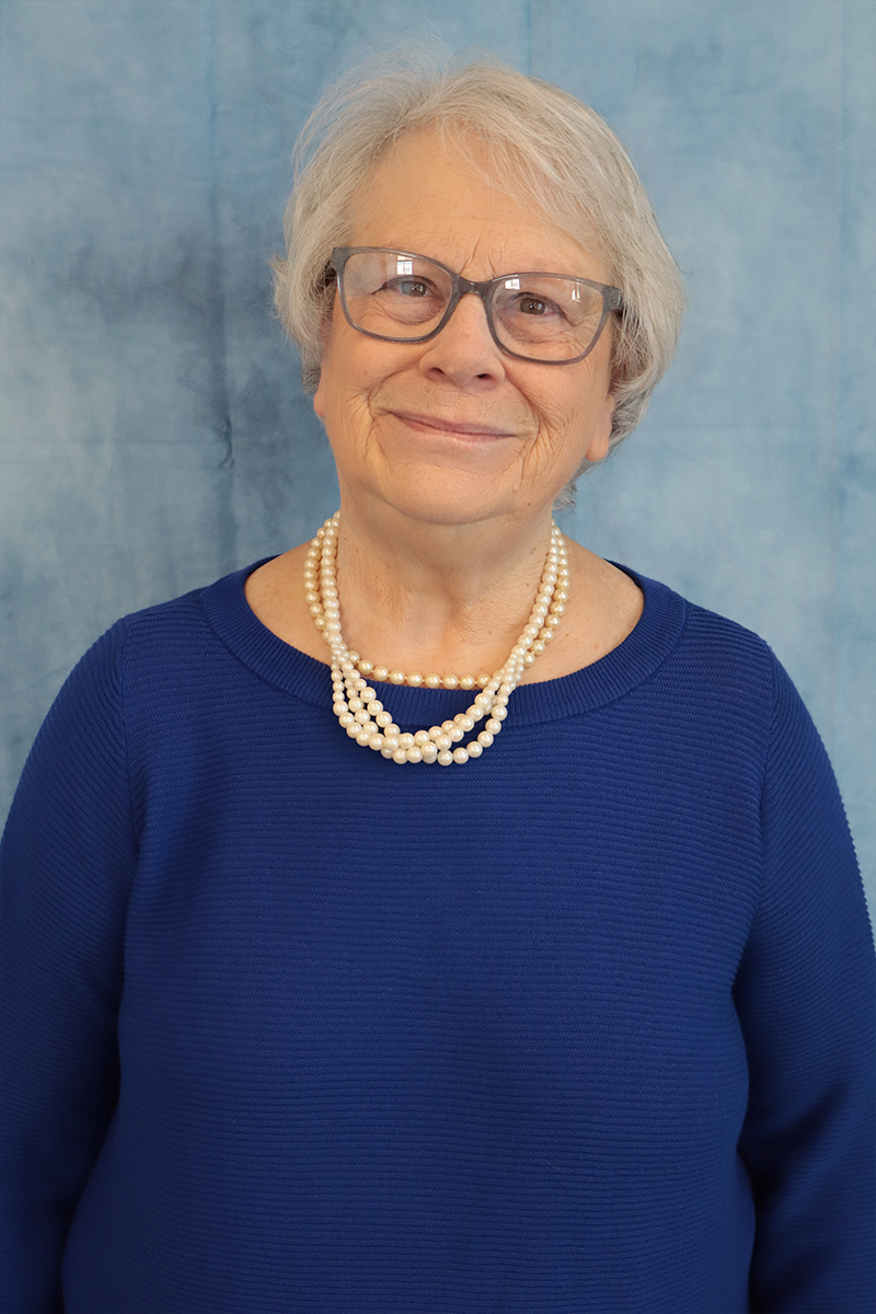 A woman wearing glasses and a pearl necklace is wearing a blue sweater.