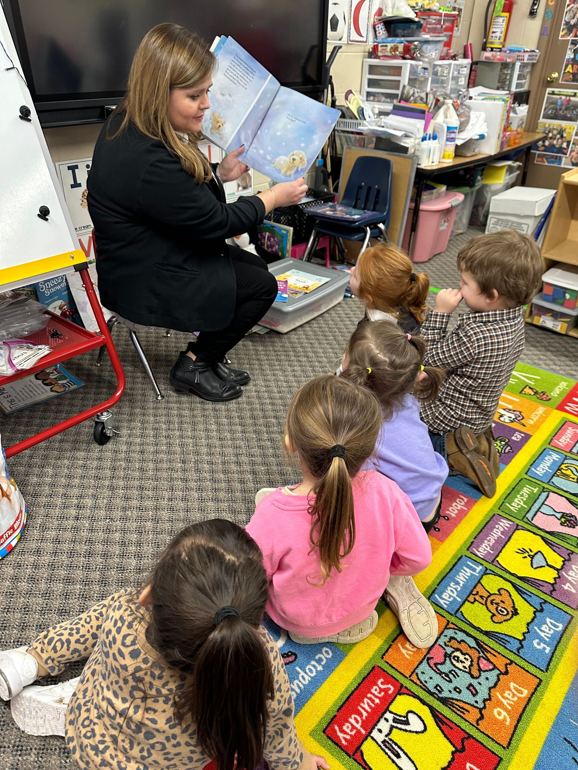 A woman is reading a book to a group of children in a classroom.