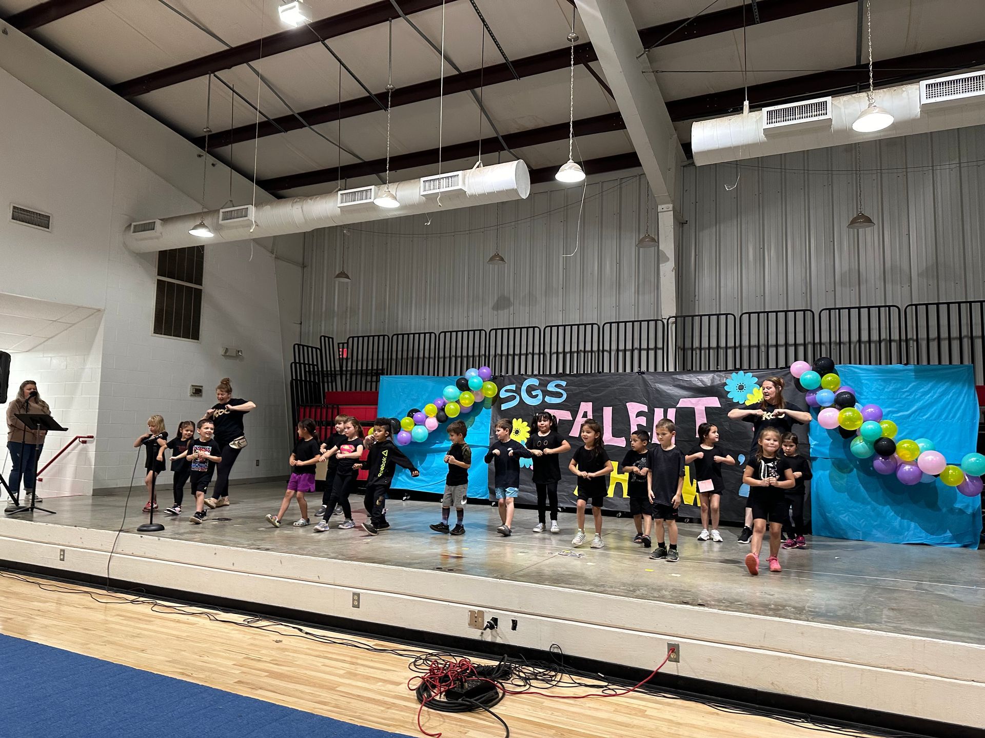 A group of children are dancing on a stage in a gym.