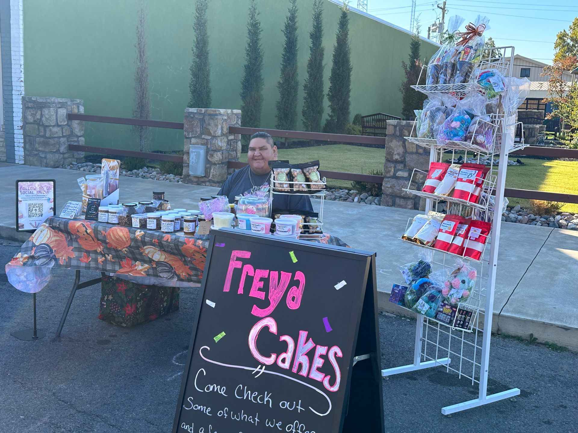 A man is sitting at a table behind a sign that says freya cakes.