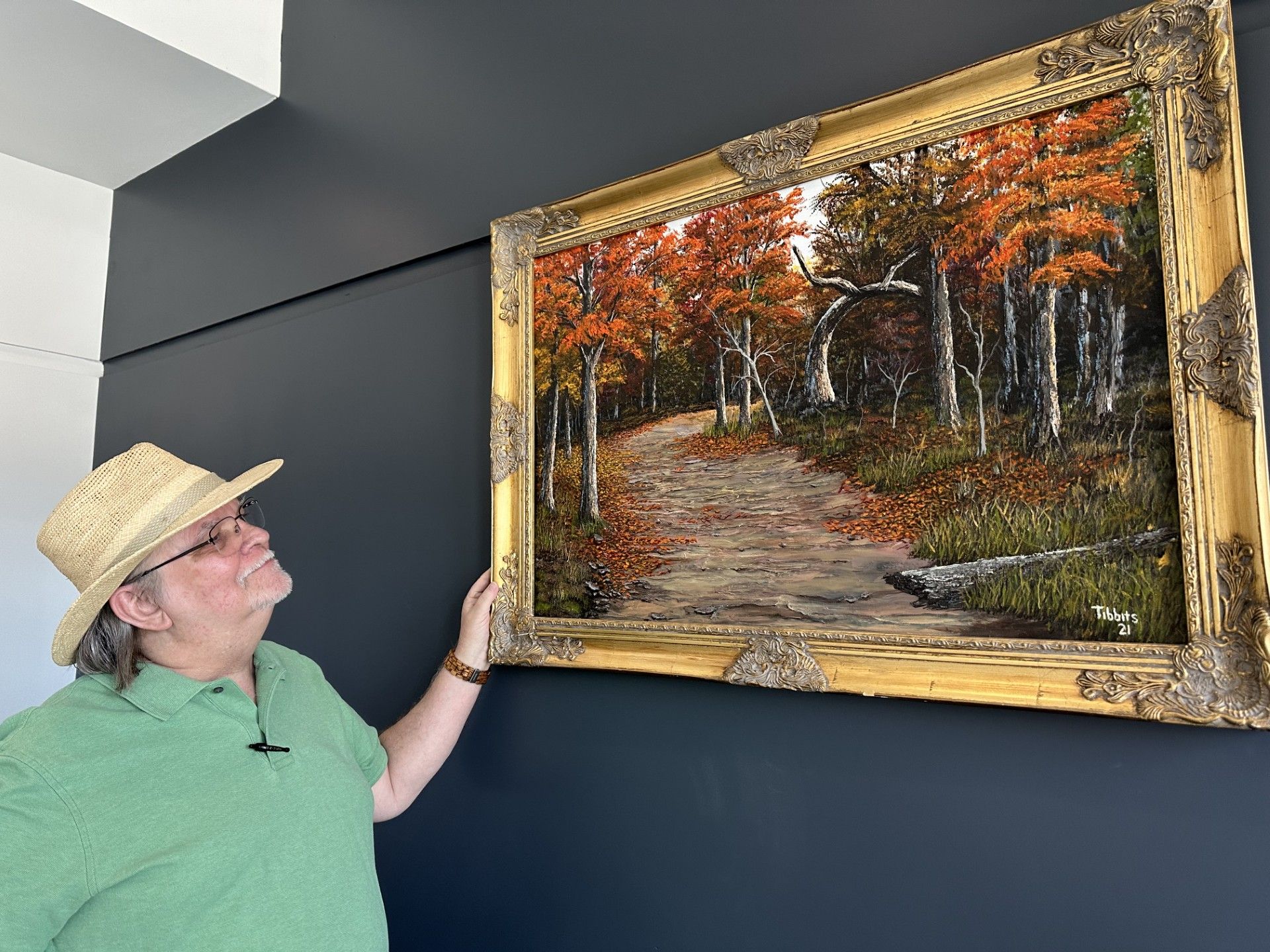 A man in a hat is looking at a painting on a wall.