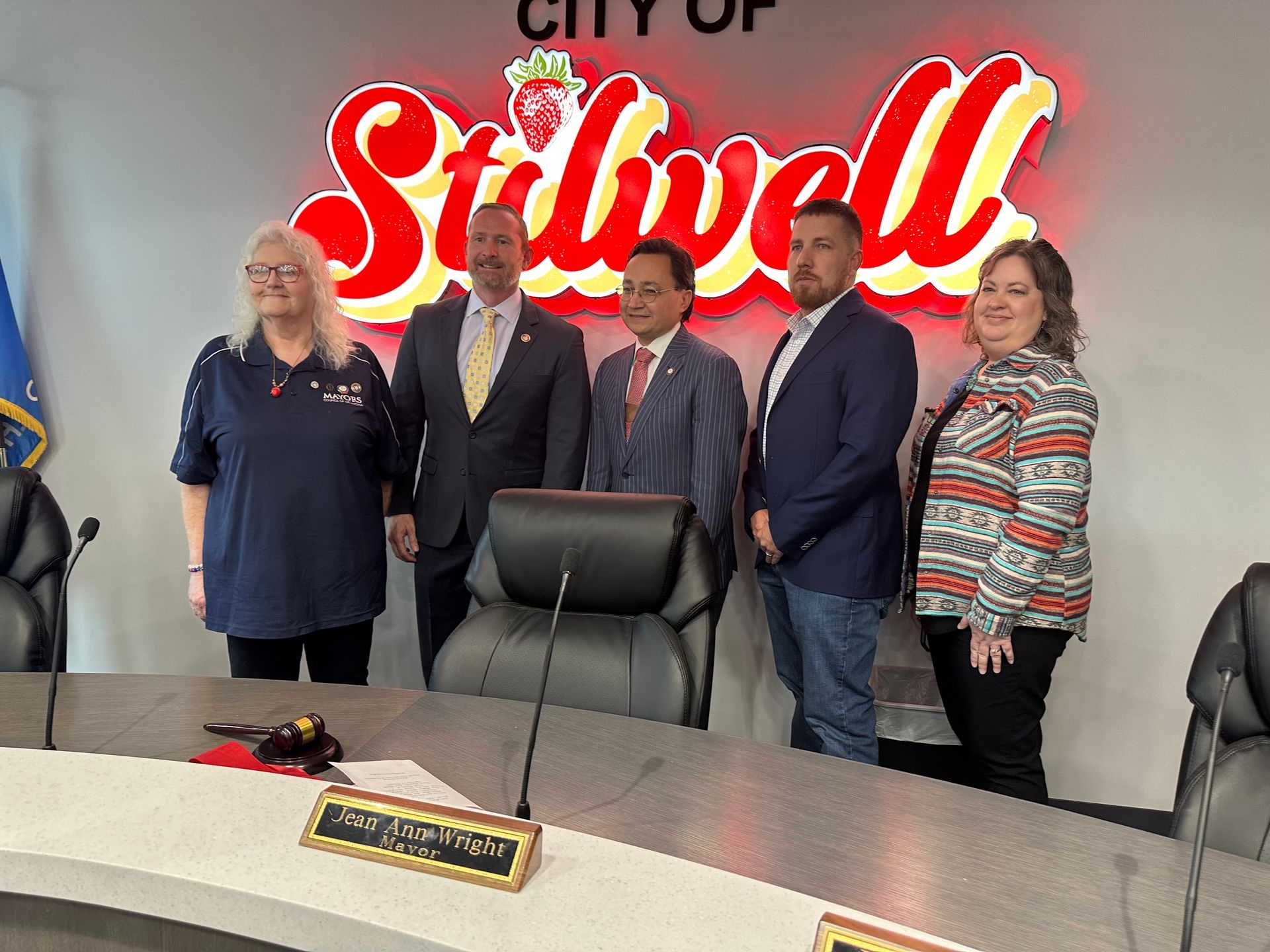 A group of people are standing around a table in front of a sign that says city of stilwell.