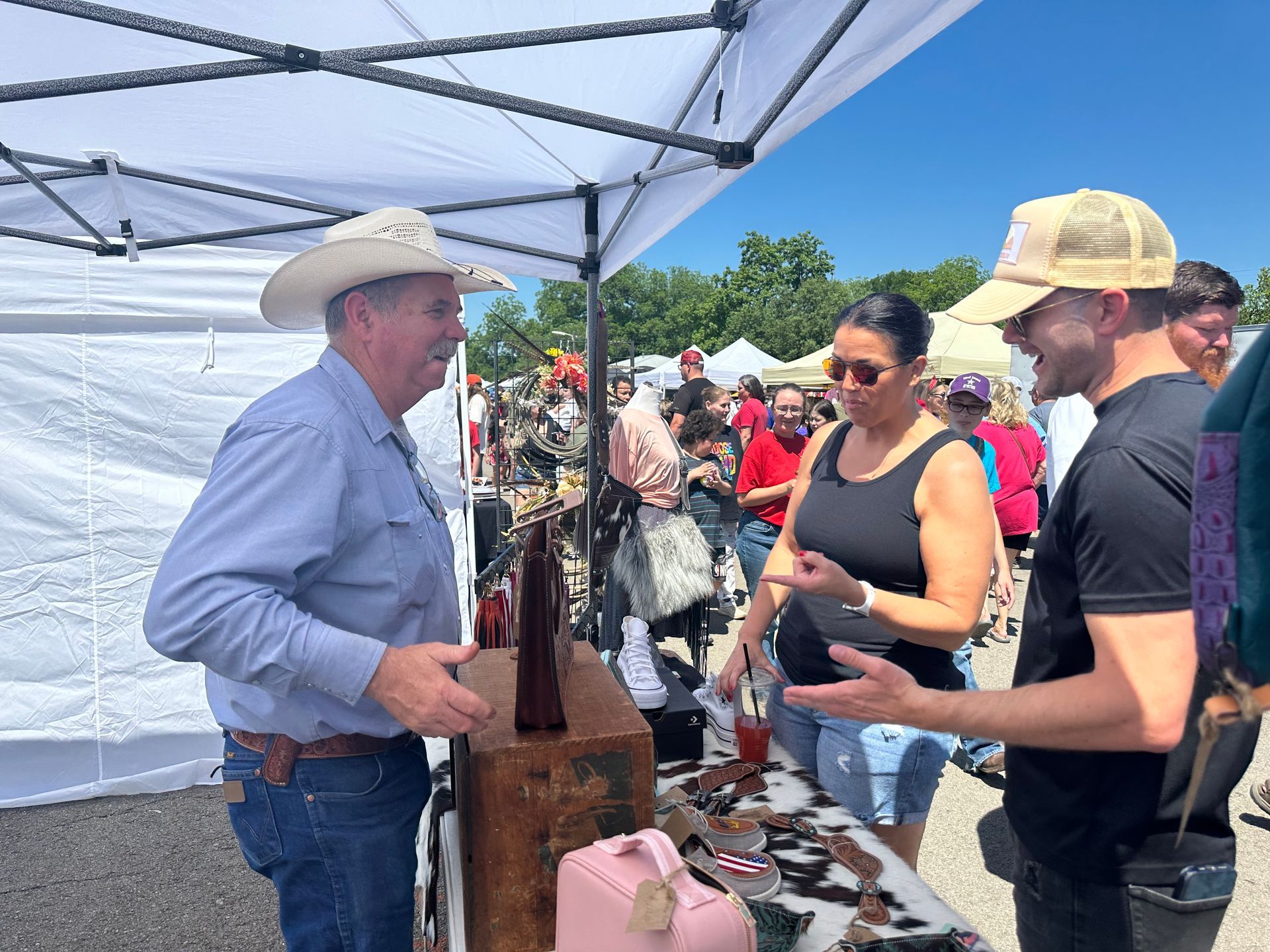 A man in a cowboy hat is talking to a woman at an outdoor market.