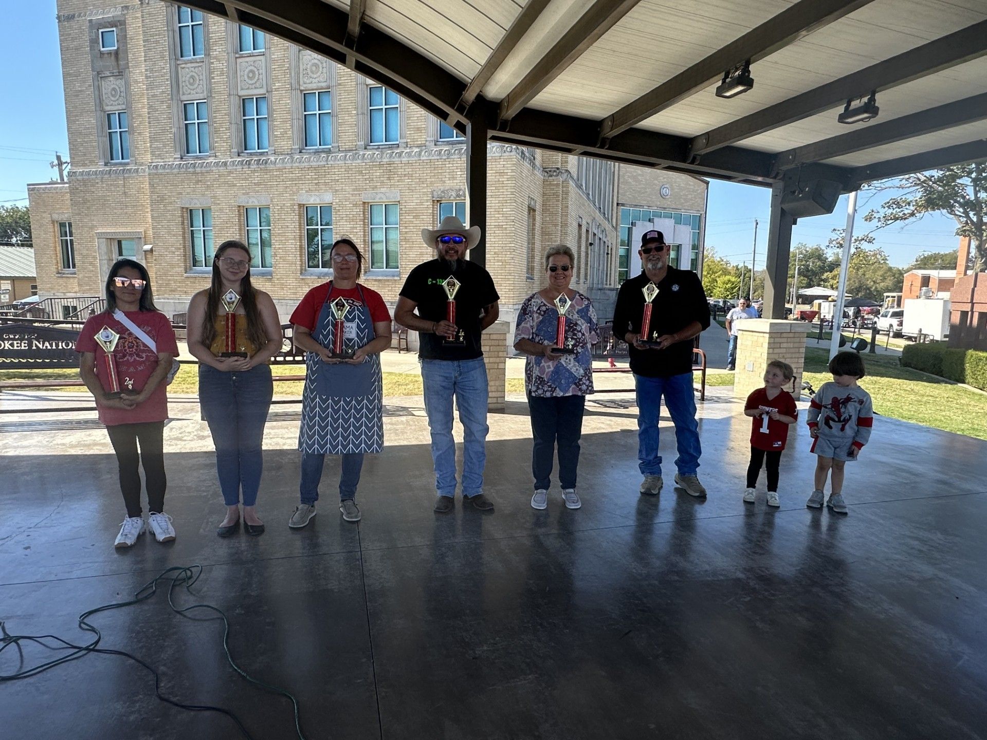 A group of people are standing under a canopy holding trophies.