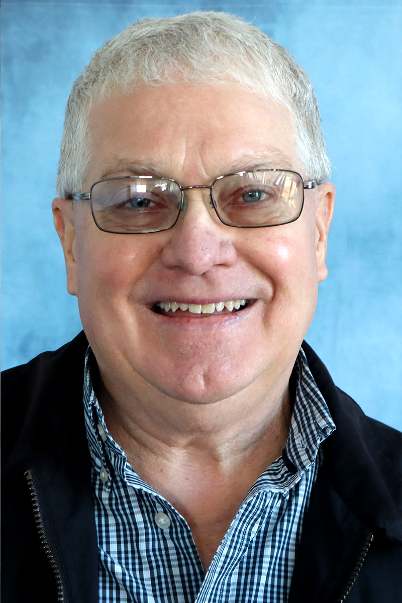 A man wearing glasses and a plaid shirt smiles for the camera
