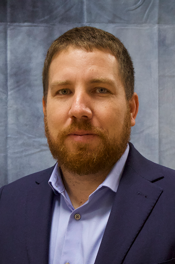 A man with a beard is wearing a suit and a blue shirt.