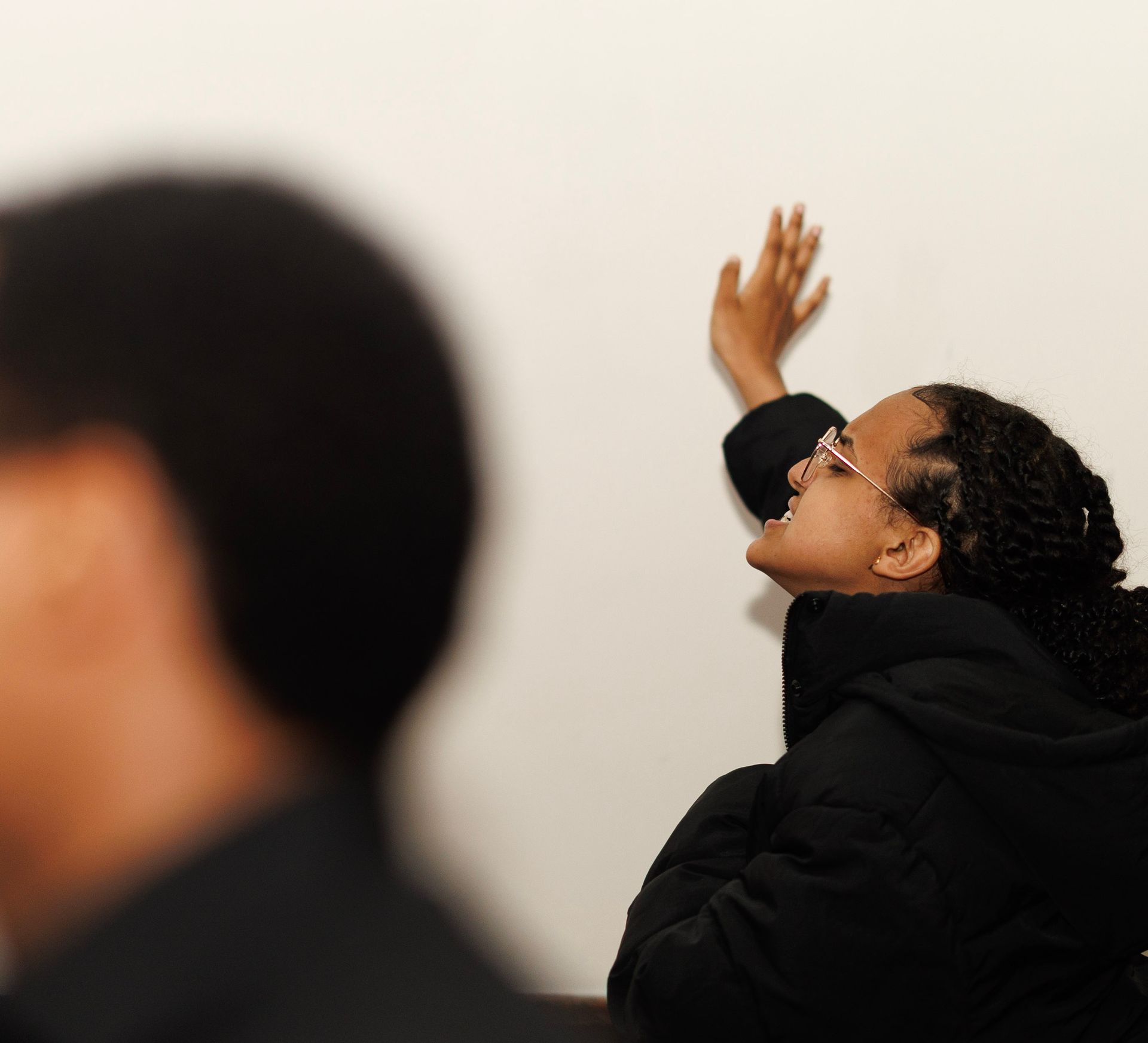 A woman wearing glasses is leaning against a wall
