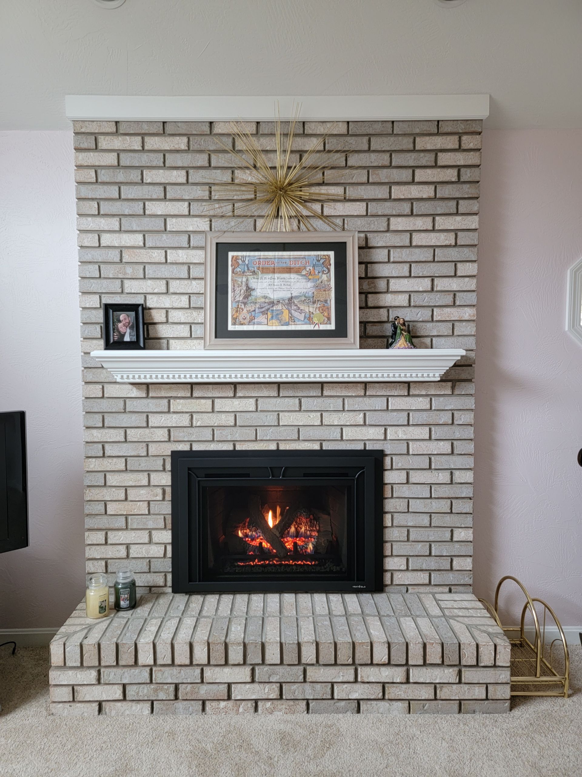 A living room with a brick fireplace and a picture on the mantle.