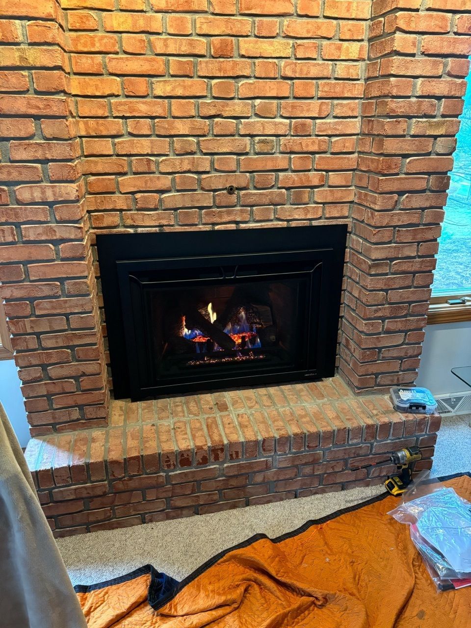 A brick fireplace with a gas fireplace insert in a living room.