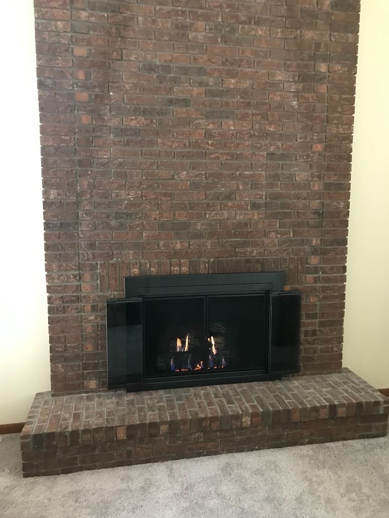 A brick fireplace with a black screen in a living room.