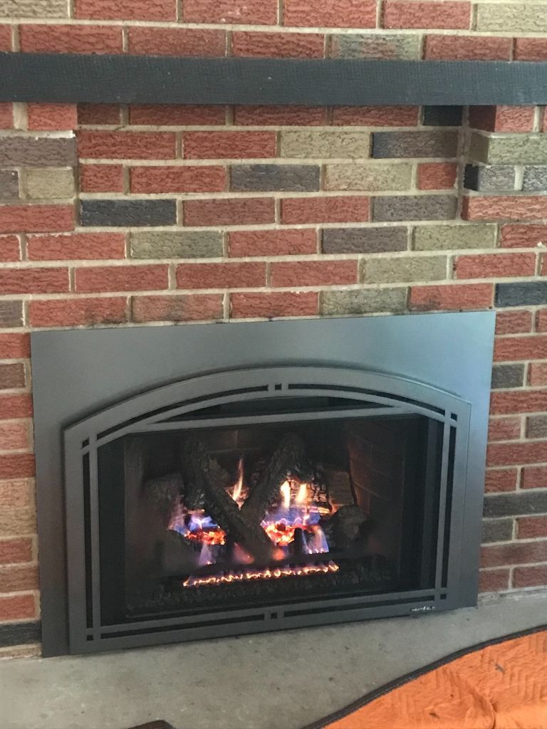 A gas fireplace is built into a brick wall in a living room.