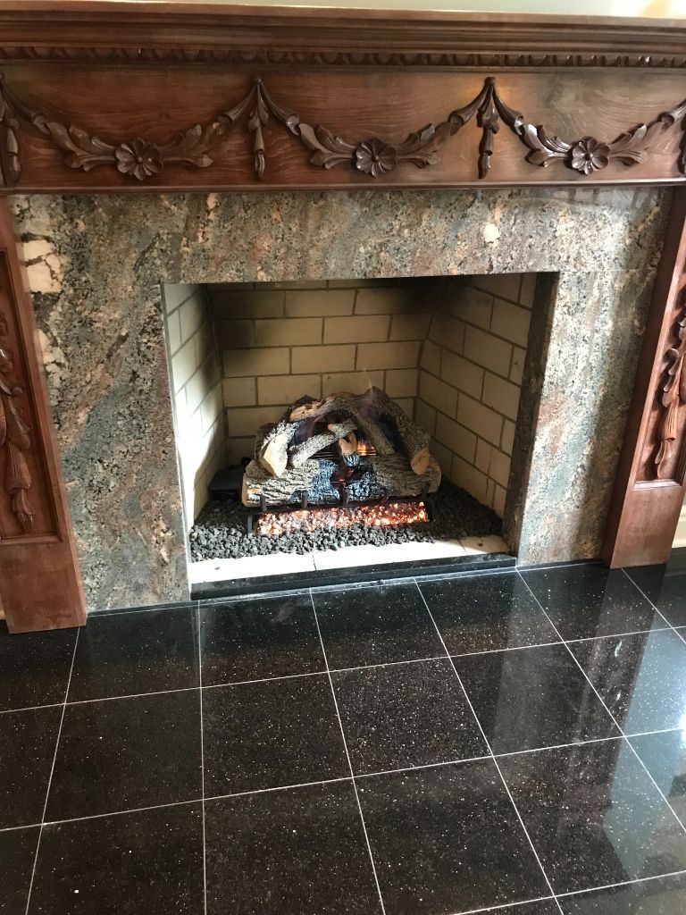 A fireplace with a wooden mantle and a black tile floor.