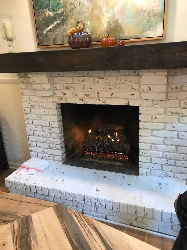 A white brick fireplace with a wooden mantle in a living room.