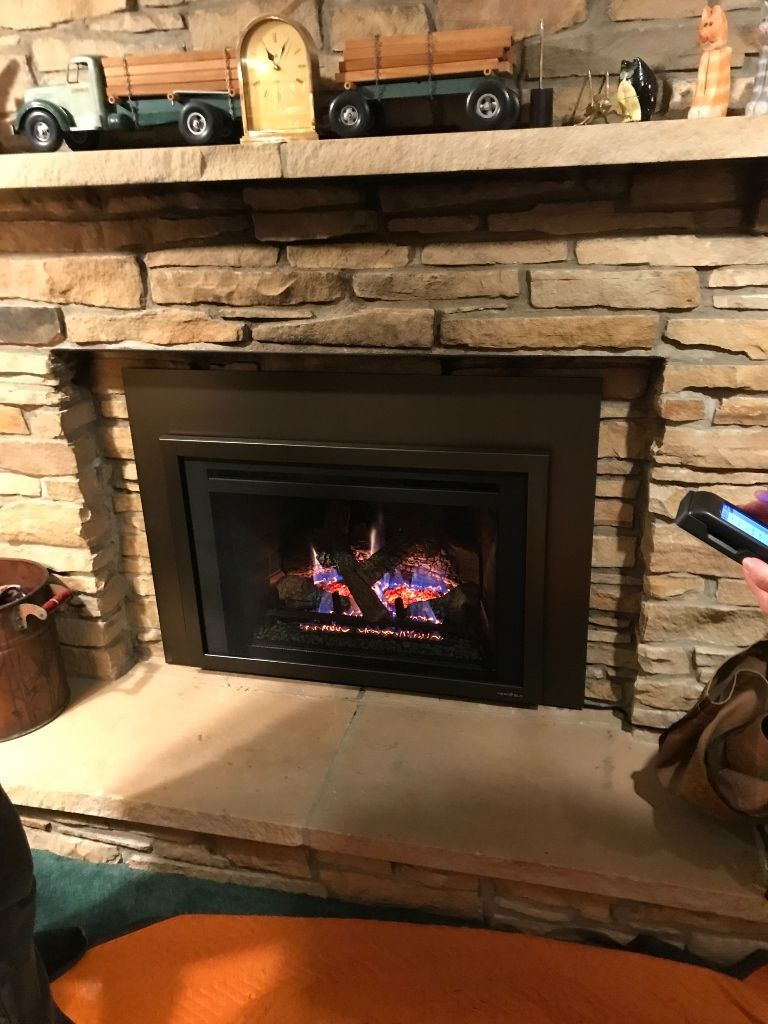 A person is holding a remote control in front of a fireplace.