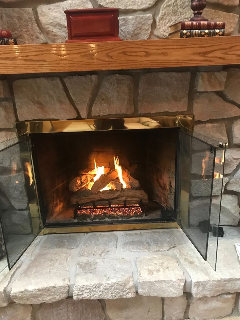 Fireplace with burning logs, set in a stone wall, with glass screens and wooden mantel.