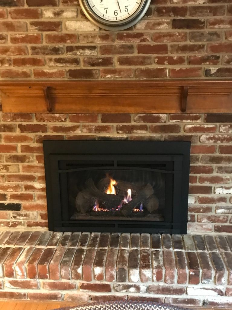 A fireplace with a clock above it and a brick wall.