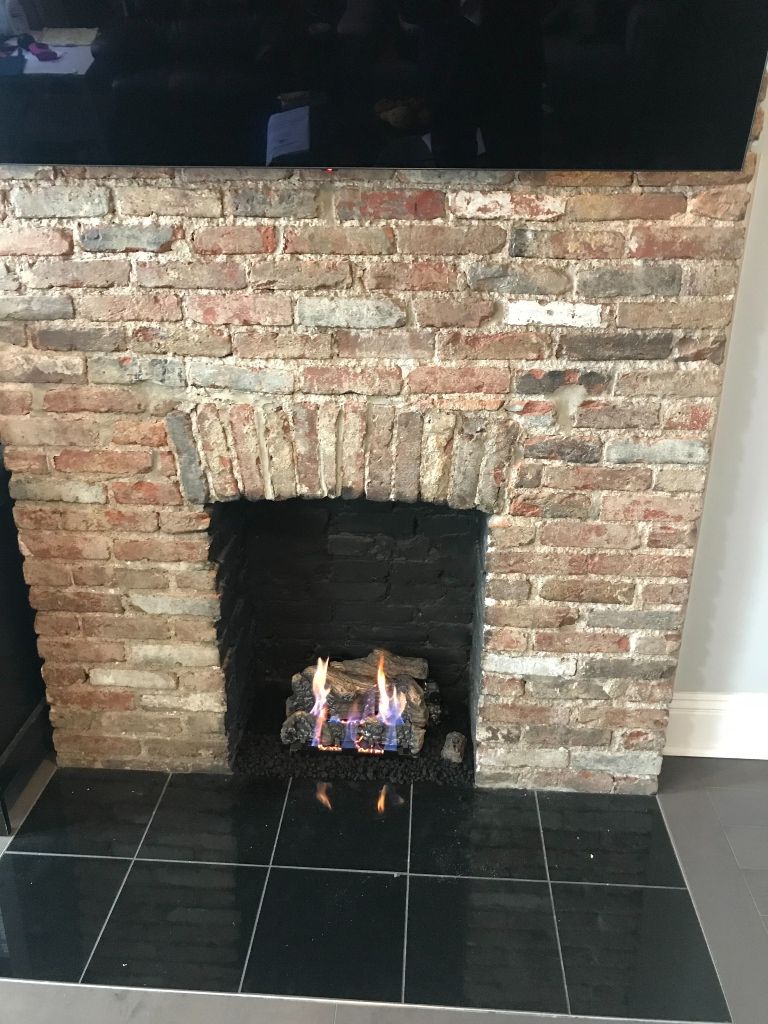 A brick fireplace with a fire in it and a black tile floor.