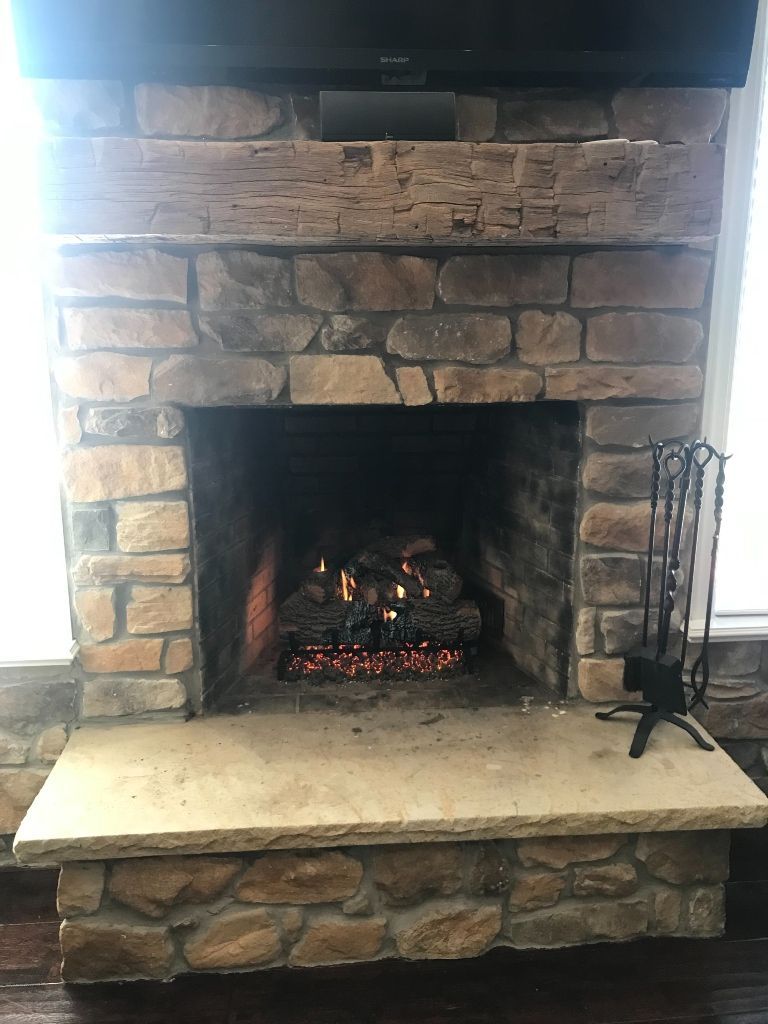 Fireplace with burning logs, stone surround, and wooden mantle; metal fireplace tools stand beside it.