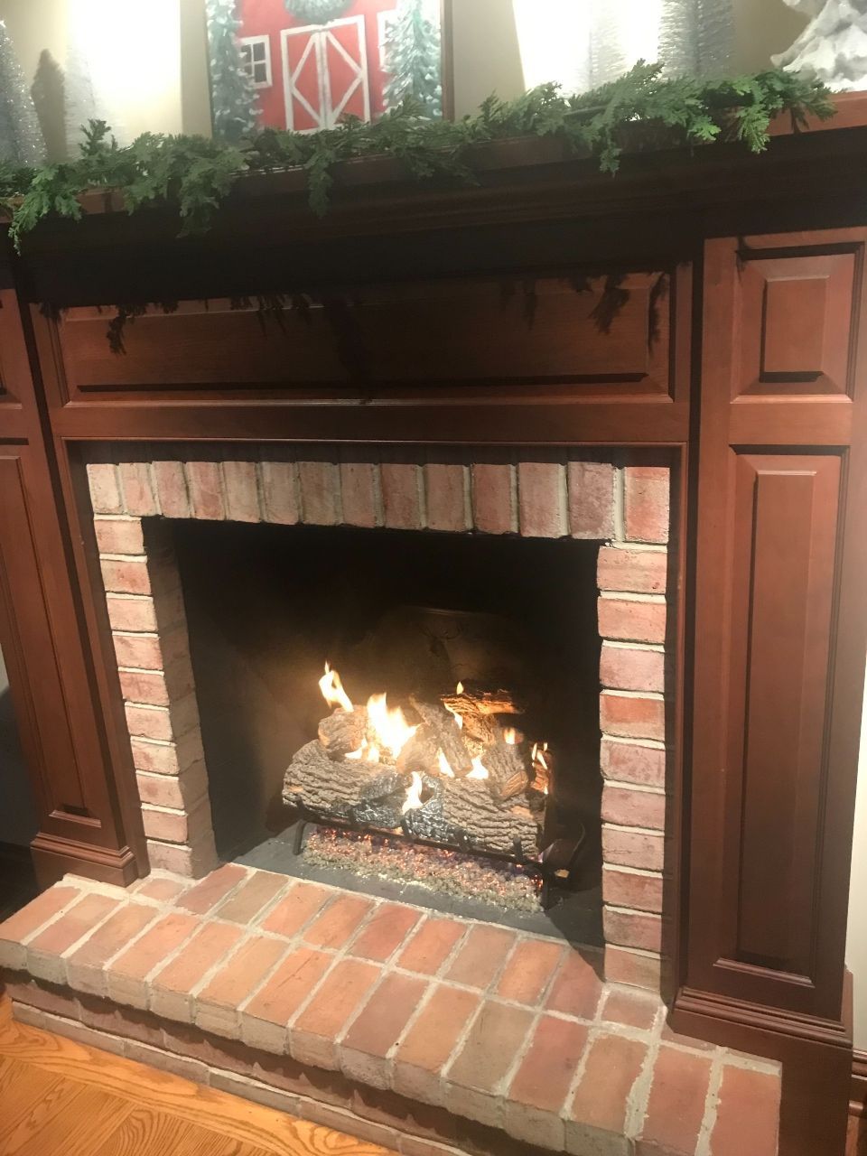 Fireplace with brick surround, wood mantle, and burning flames. Decorated with greenery.