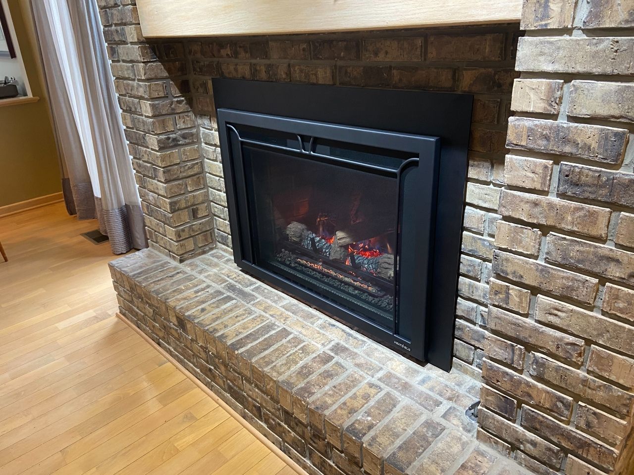 A brick fireplace with a black fireplace insert in a living room.