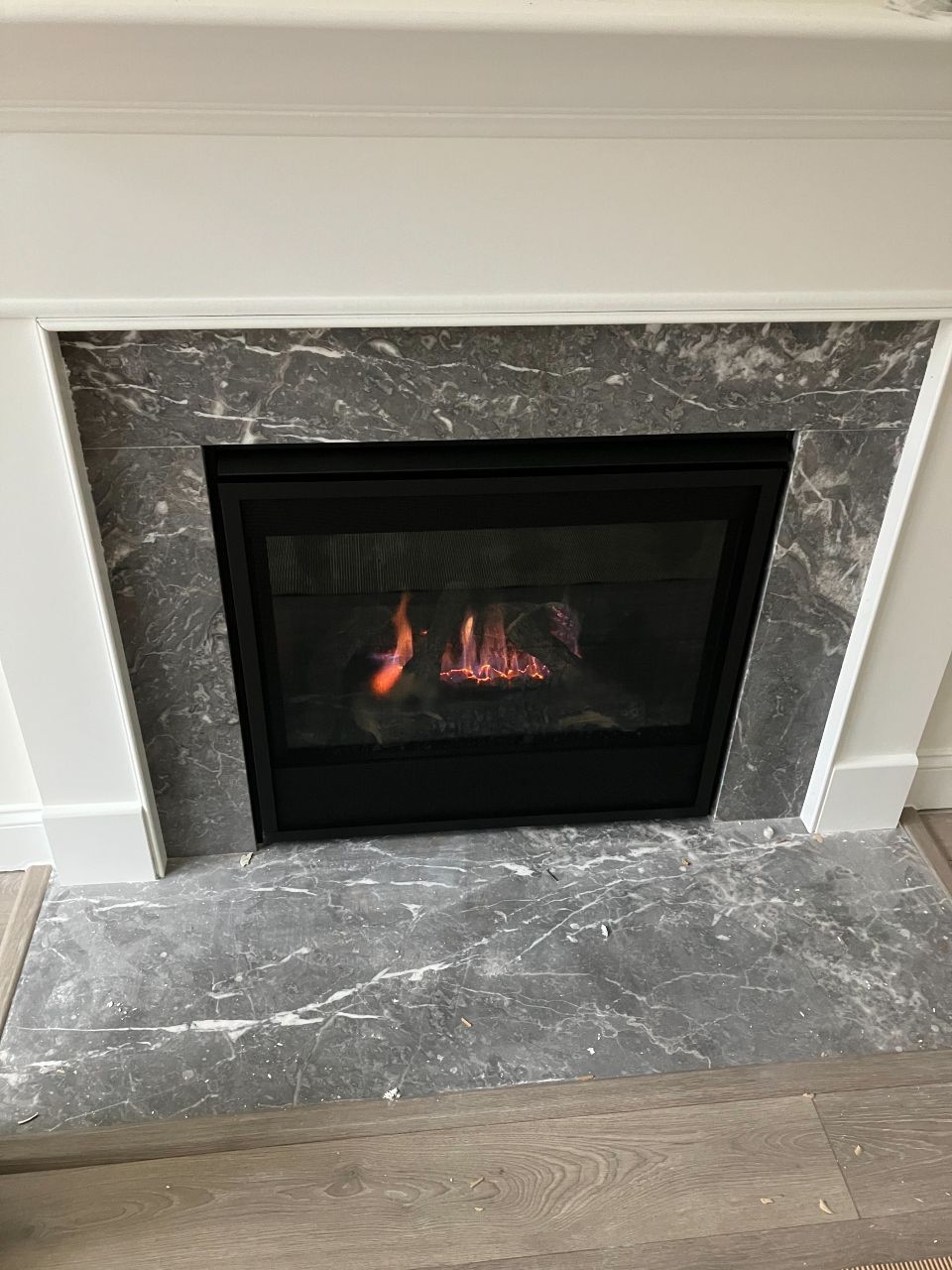 A fireplace with a gray marble surround and white mantel; flames burning inside.
