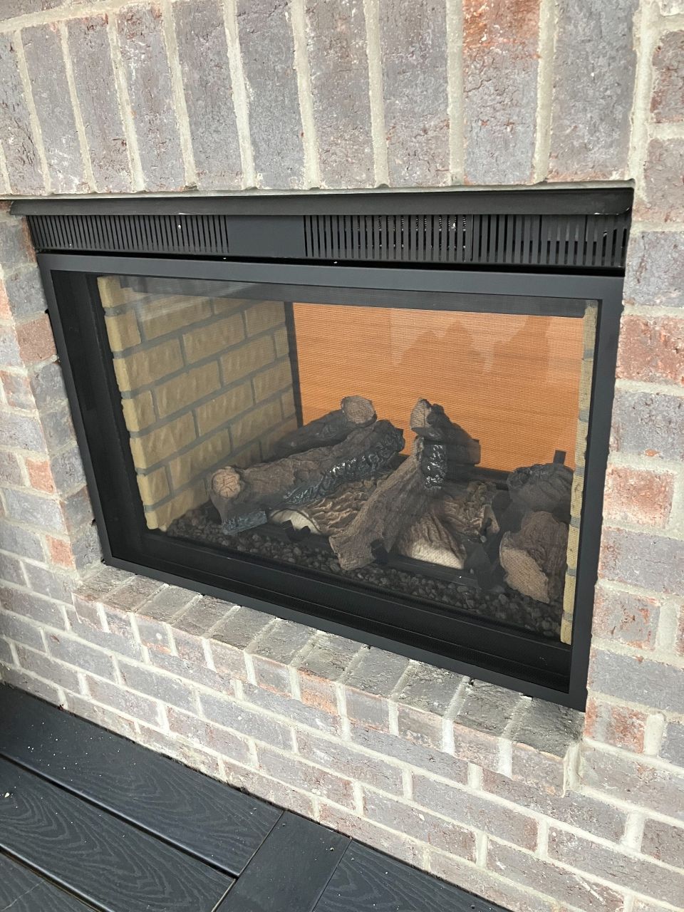 A fireplace with logs in it is built into a brick wall.
